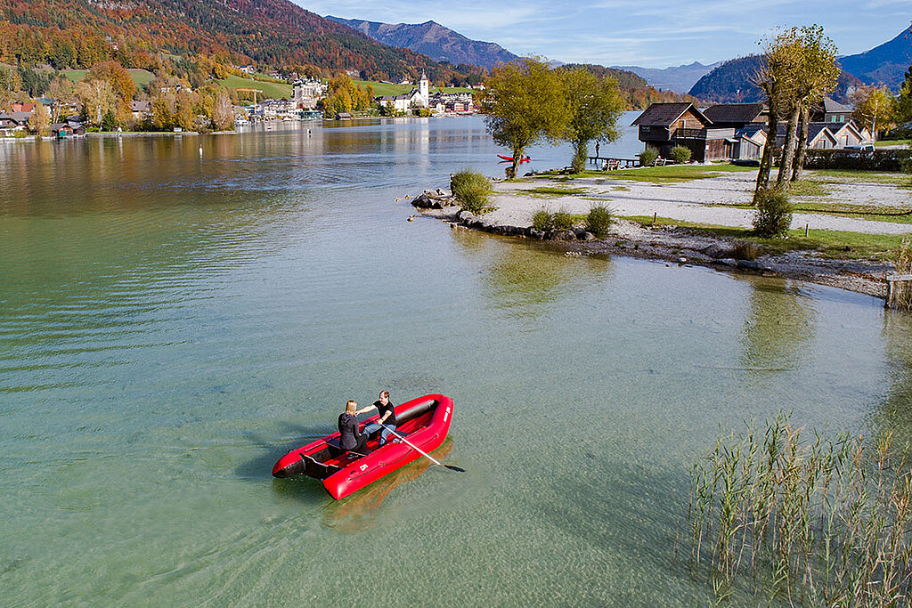 Pärchen fährt mit seinem Elektromotor-Schlauchboot am Flussufer entlang