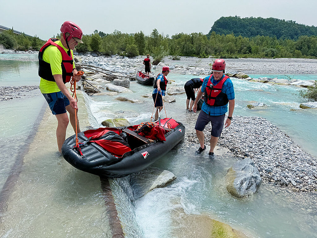 Eine Gruppe von Personen tragen ein Schlauchboot über eine Stromschnelle im Fluss 